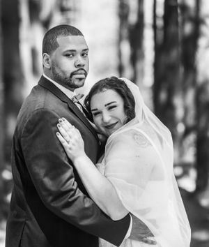 Elegant black and white portrait of bride and groom embracing tenderly among tall trees.