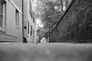 Low angle black and white view down narrow cobblestone alley between brick walls.