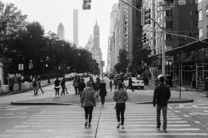 People walking across a busy Manhattan intersection with tall skyscrapers in the background.