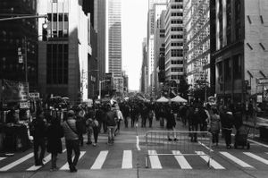Crowded New York City street scene with pedestrians crossing at a crosswalk between tall buildings.
