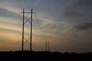 Silhouetted power lines against a golden sunset sky with dramatic clouds.