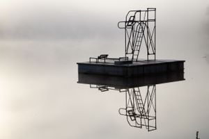 Diving platform silhouette creating perfect mirror reflection on still water.