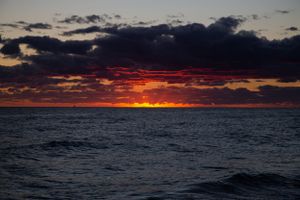 Vibrant red and orange sunset over dark ocean waters with dramatic storm clouds.