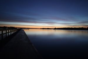 Long wooden pier extends into still waters under a dusky twilight sky.