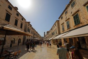 Historic limestone shopping street with awnings and tourists in Dubrovnik's old town.