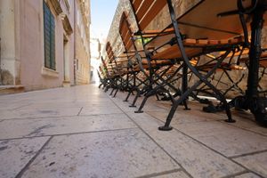 Row of stacked cafe chairs and tables along a stone paved street in an old European city.