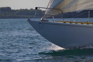 Close-up of a sailboat bow cutting through blue water creating white spray.
