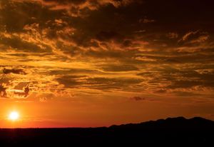 Dramatic orange sunset with silhouetted mountains beneath dark cloudy skies.