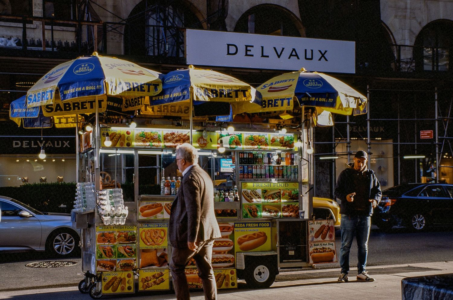 Street food vendor cart with blue umbrellas and Delvaux signage on urban sidewalk.