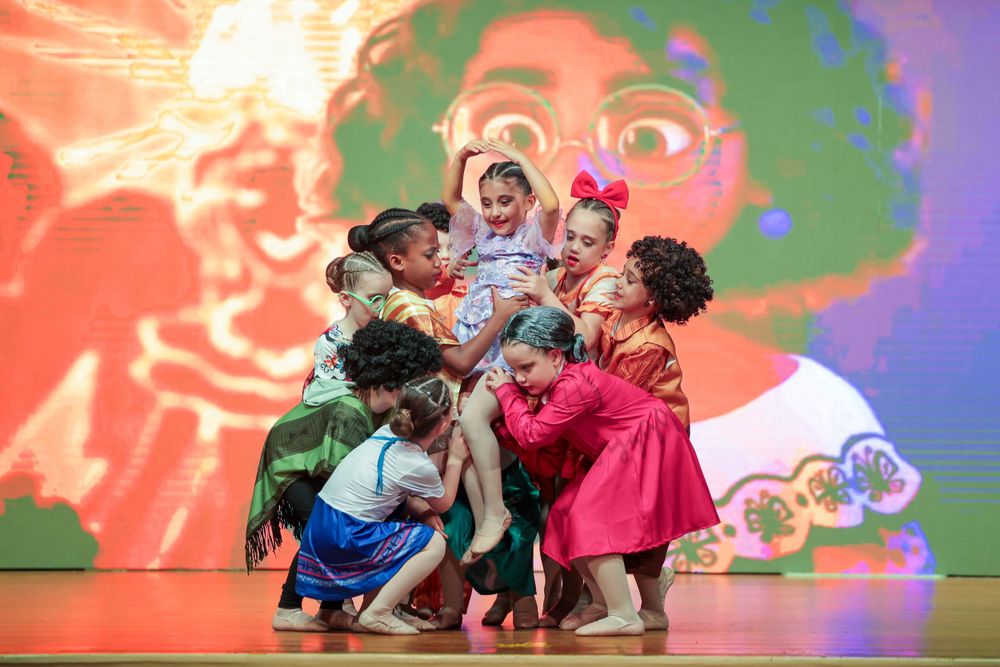 Dance ensemble performs theatrical choreography against a vibrant orange projected backdrop.