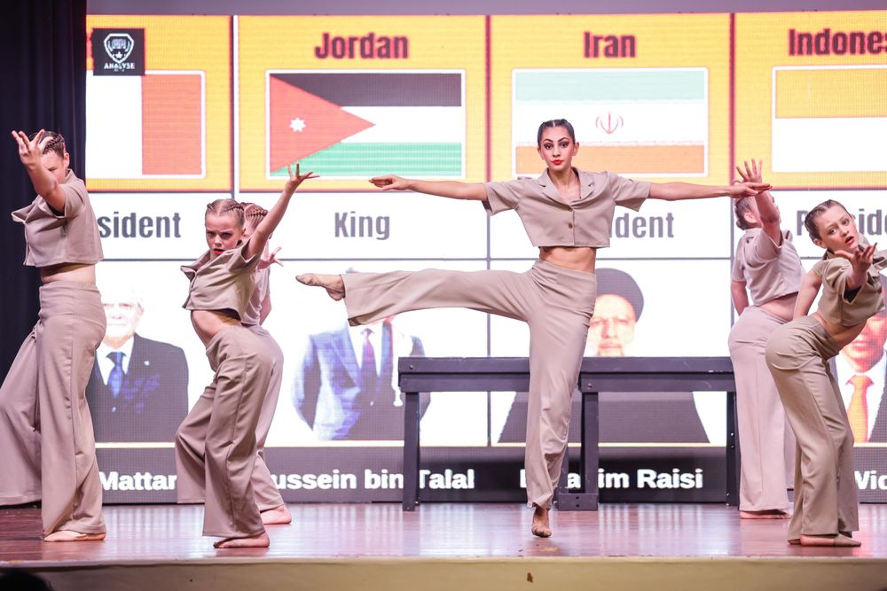 Contemporary dance ensemble performs coordinated movements with Middle Eastern flags displayed behind them.