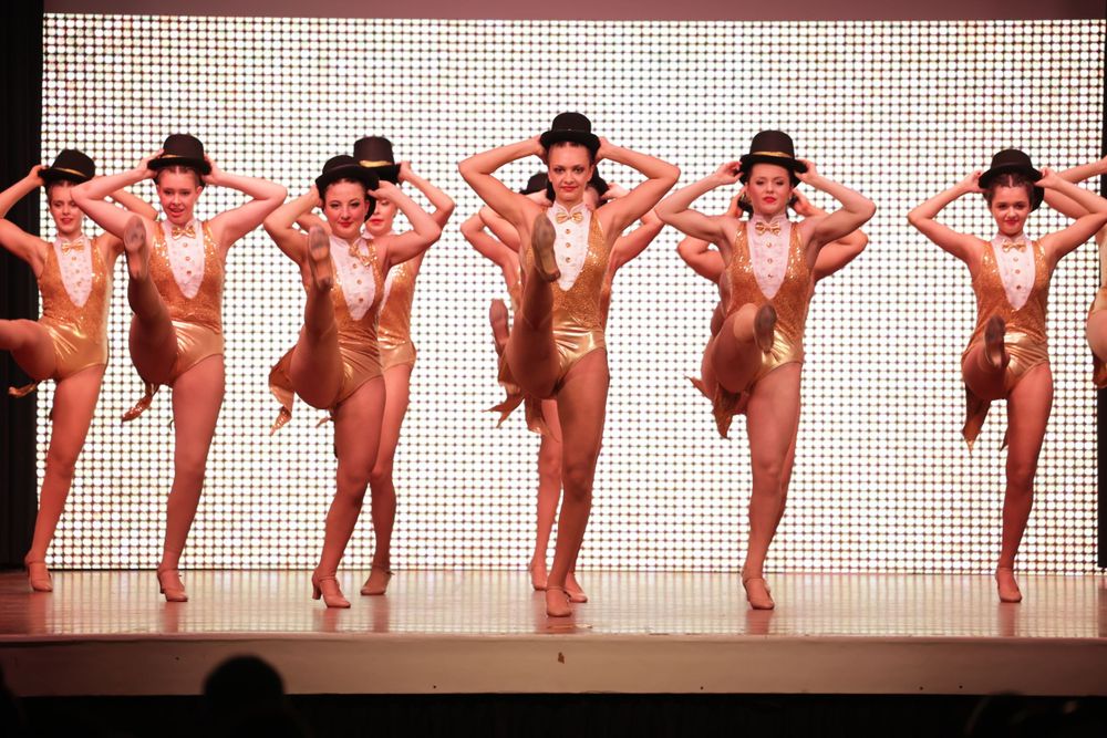 Dancers strike identical poses in matching costumes during a synchronized stage performance.