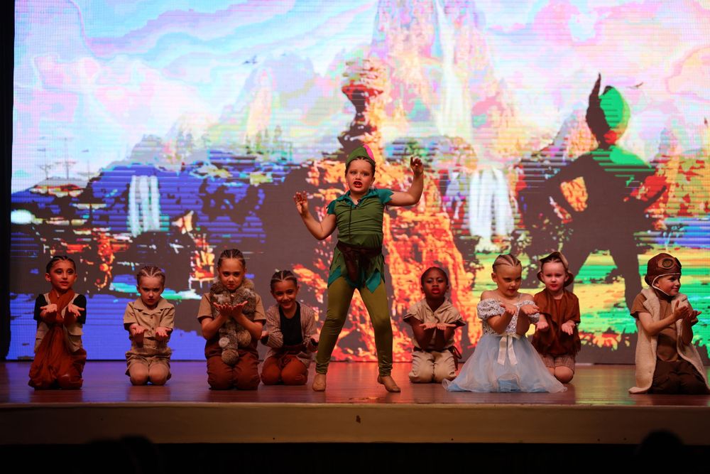 Stage performance featuring colorful animated fantasy backdrop with dancers in costume.