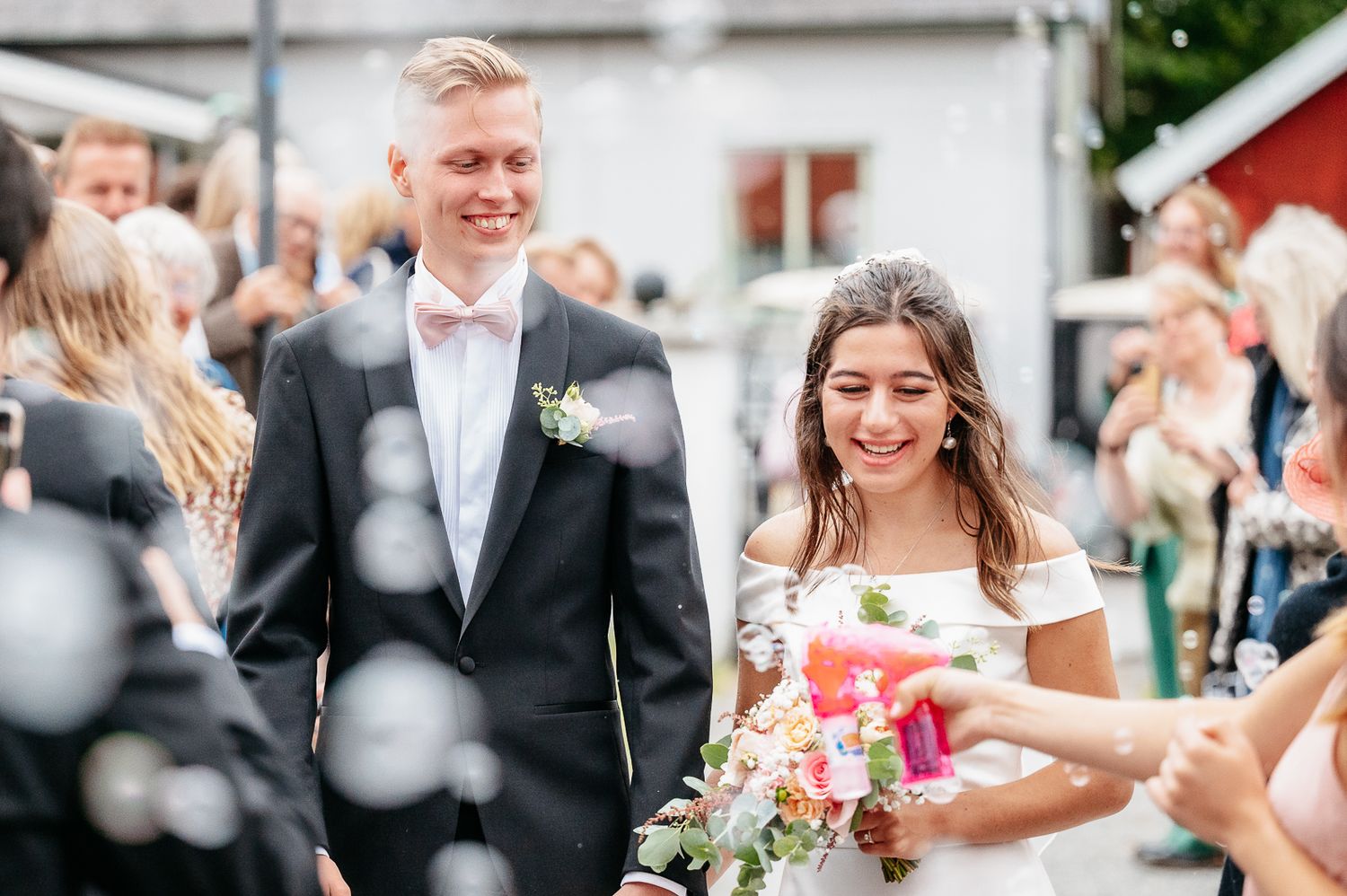 A happy couple shares a candid moment while sitting together on a wooden bench in their formal wedding attire.