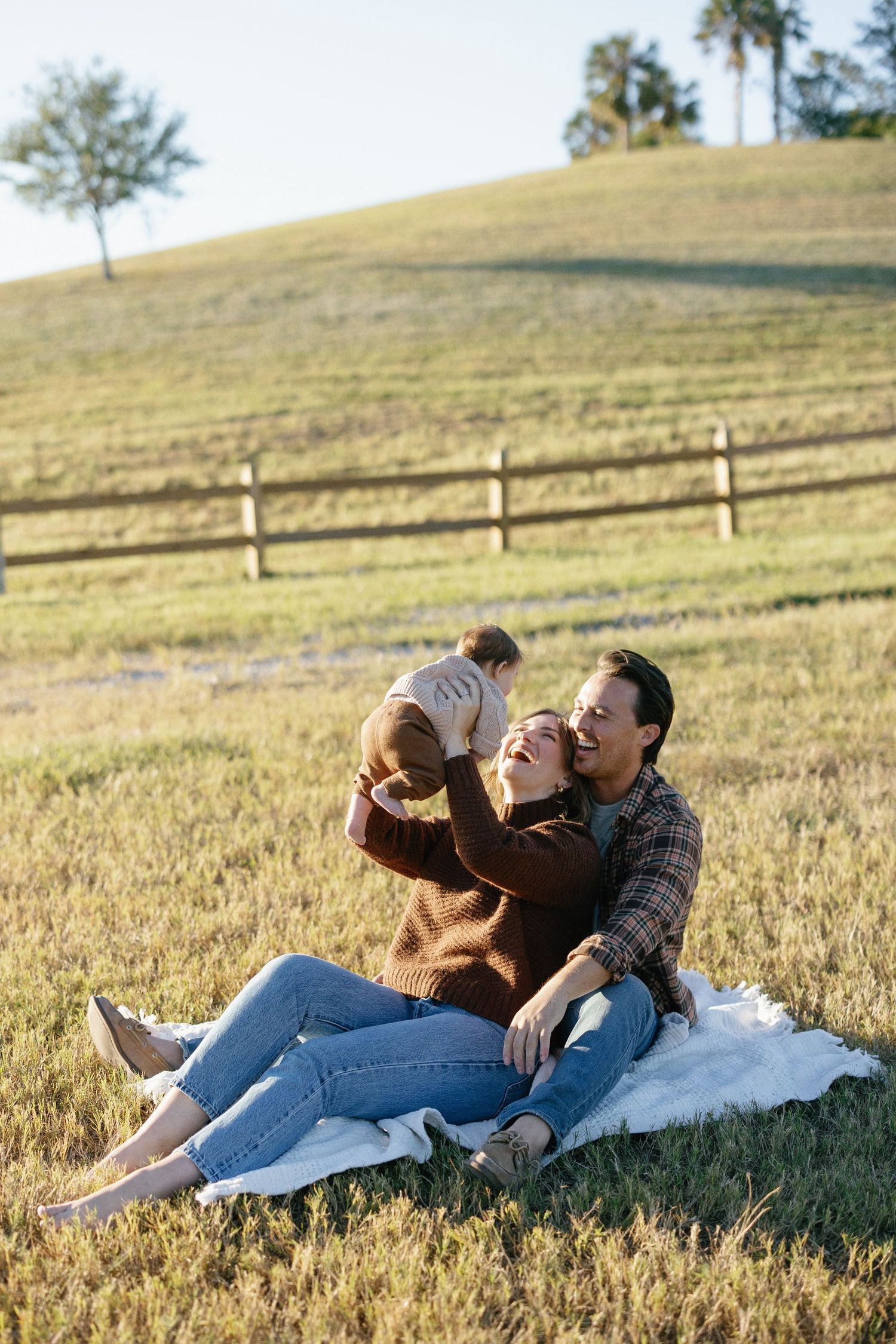 Romantic pregnant couple in white clothing pose together in a dreamy beach scene with sand dunes and sea grass at sunset.
