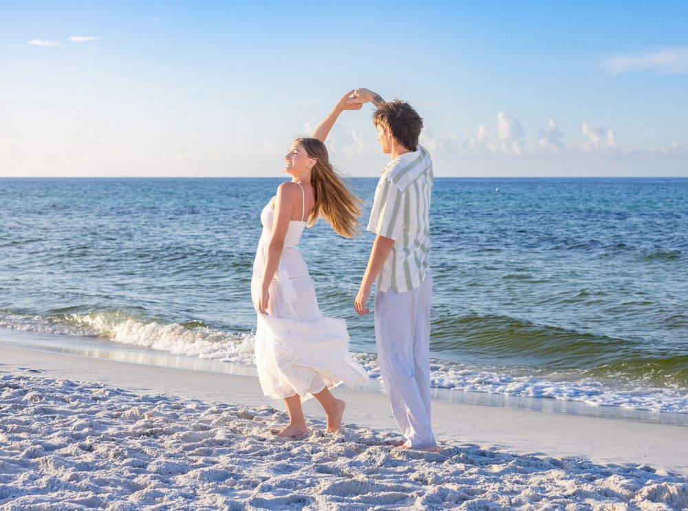 Two people walk hand in hand along the shoreline of a white sandy beach with gentle waves rolling in.