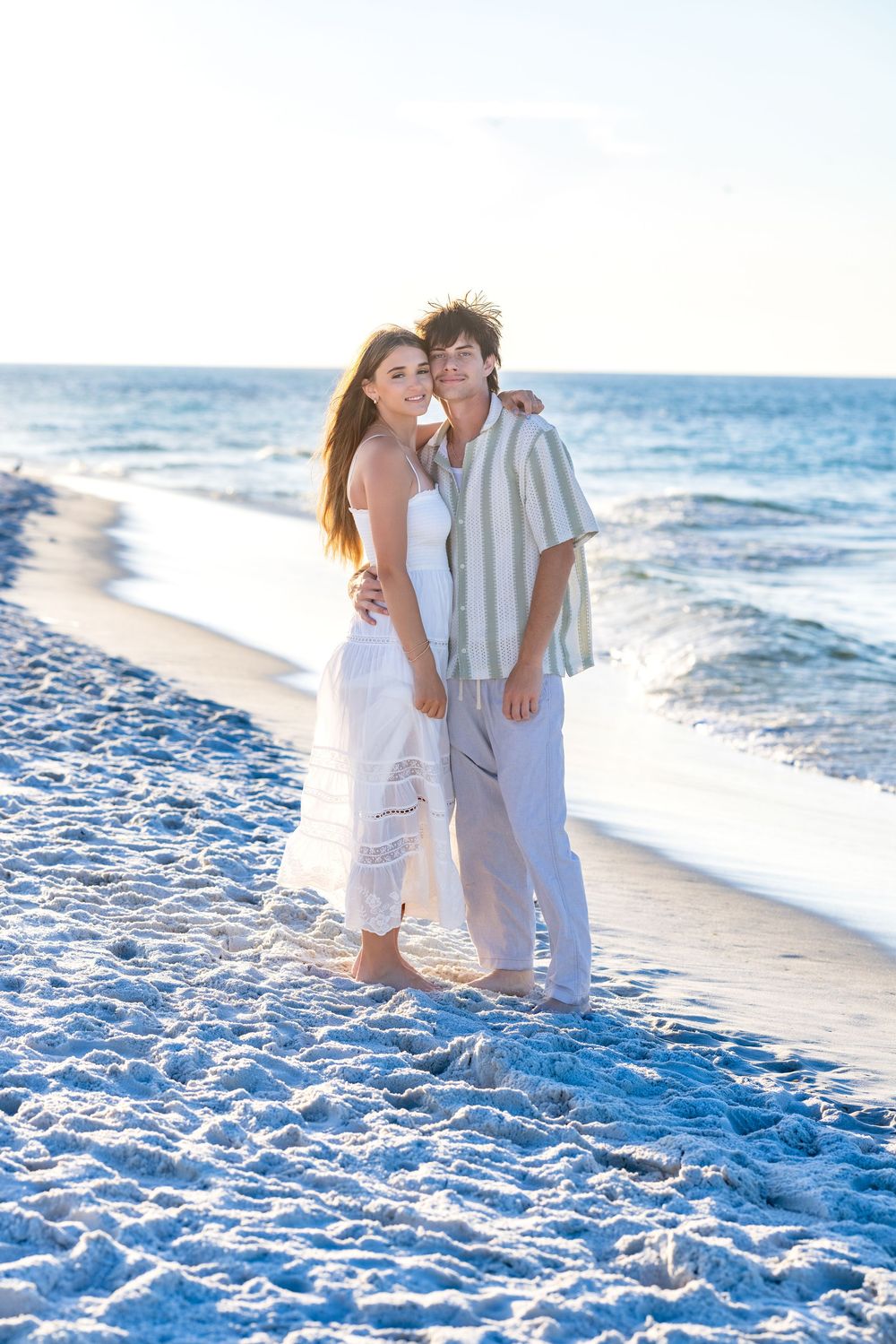 A romantic scene unfolds as two people share tender moments on a pristine beach at golden hour.