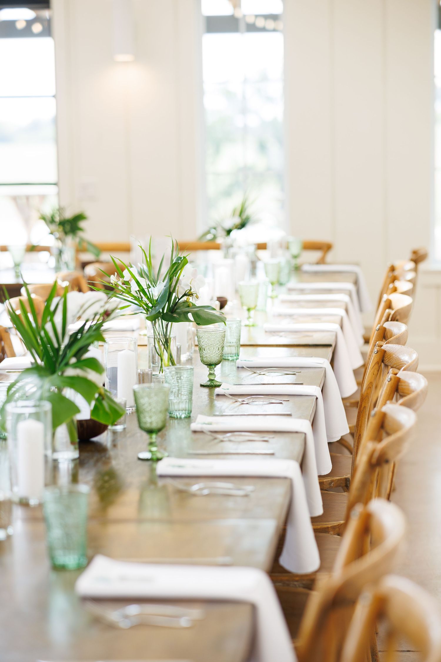 Modern table setting with white linens, wooden chairs and green glass vases filled with simple botanical centerpieces at Bella Cavalli
