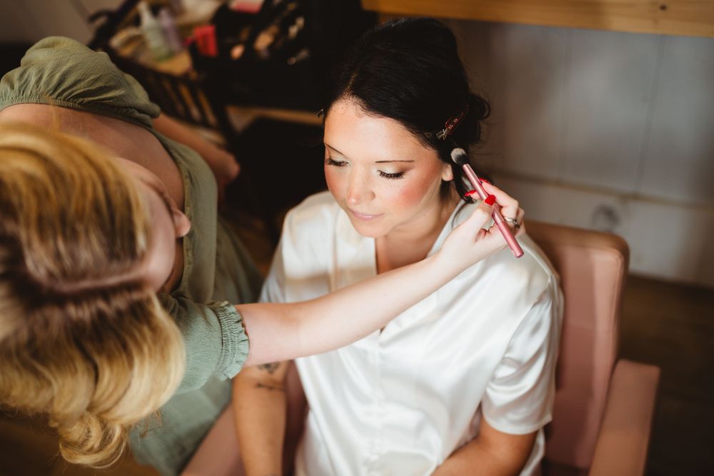 A person getting makeup applied while wearing a white robe during wedding preparations.