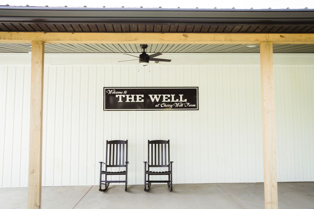 Two wooden rocking chairs sit beneath a sign reading 'The Well' on a white porch with a ceiling fan.