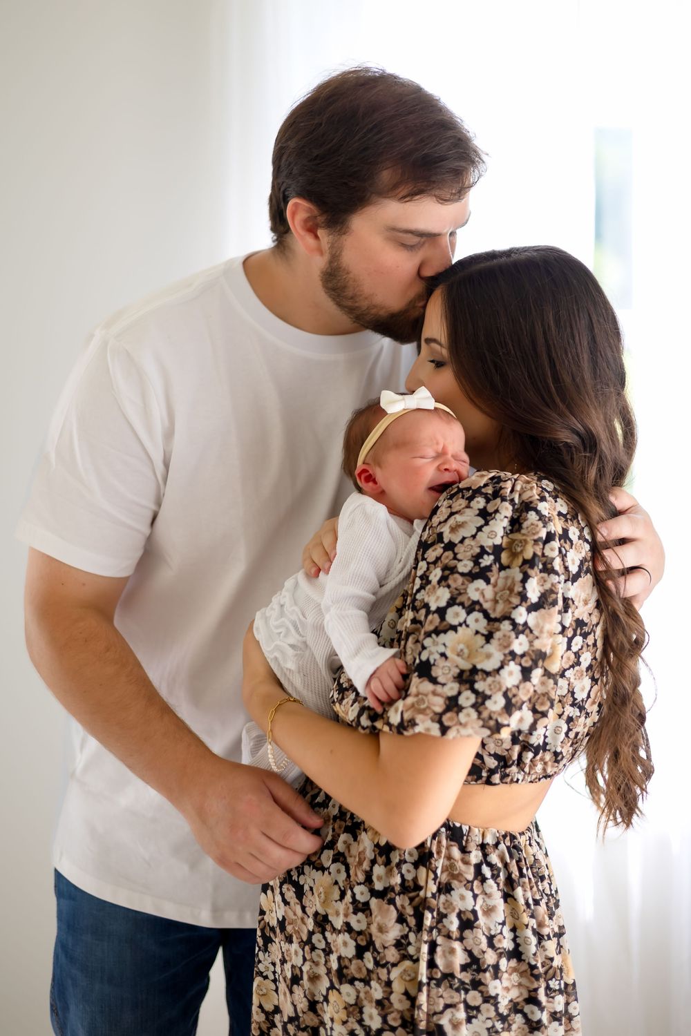 Mom and dad snuggle with baby near window during newborn session at Prospect Farms near Athens, GA