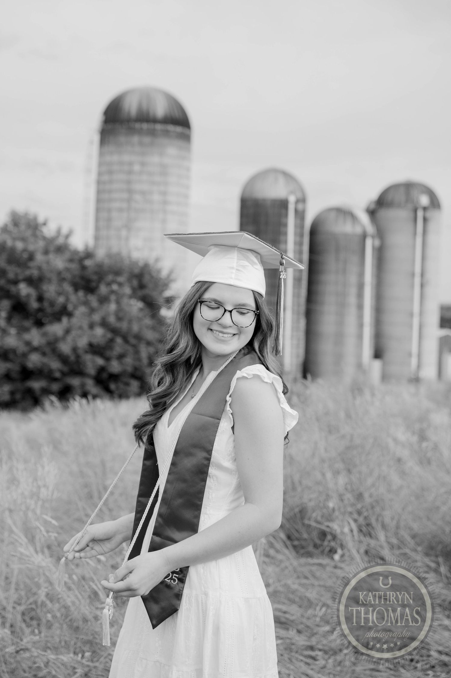 Black and white rural farm photo with tall grain silos and tall grass in foreground.