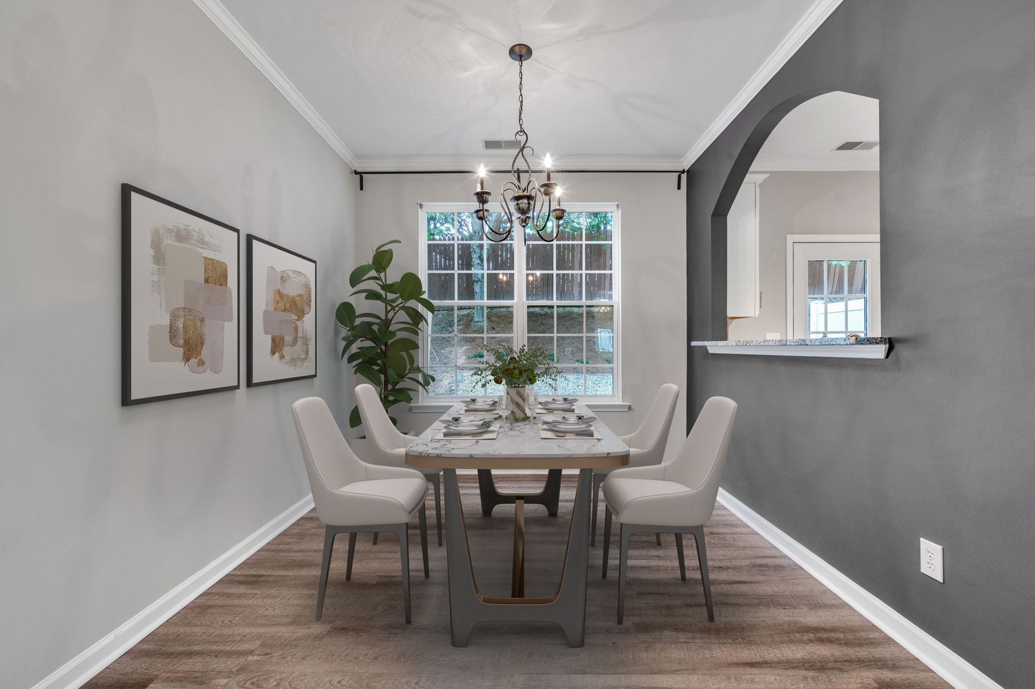 Elegant dining room with crystal chandelier, gray walls, and large window.