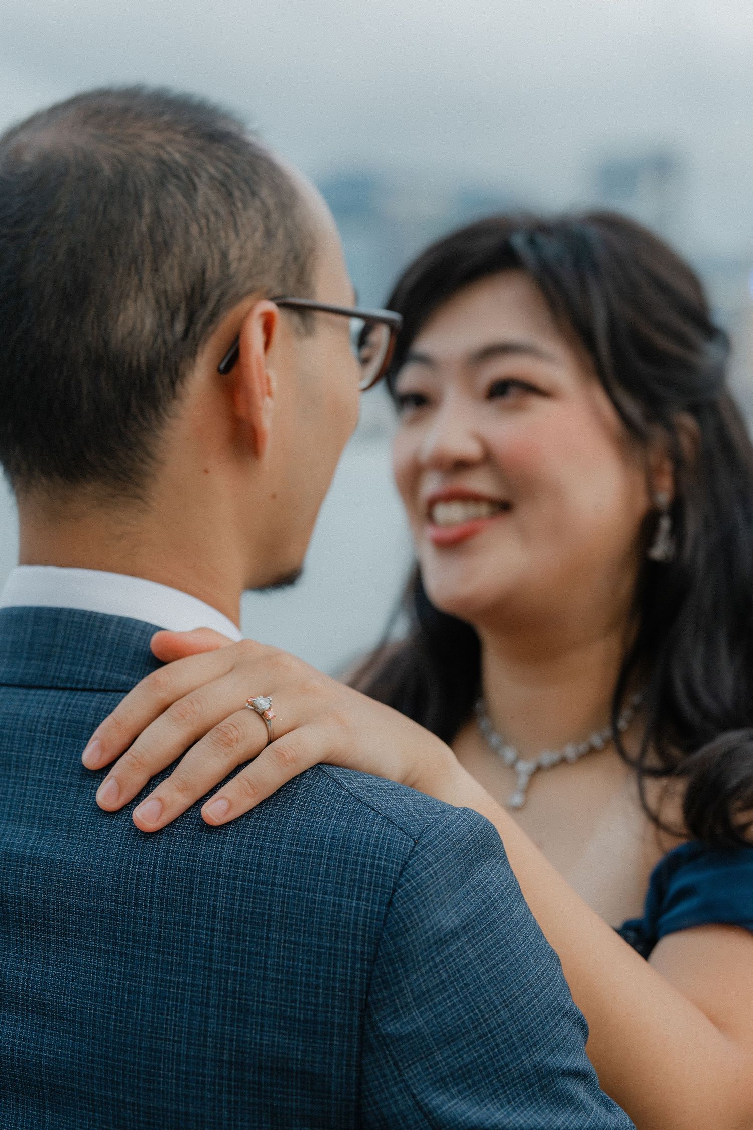 A romantic couple shares an intimate moment as she smiles while placing her hand on his shoulder showing her ring.