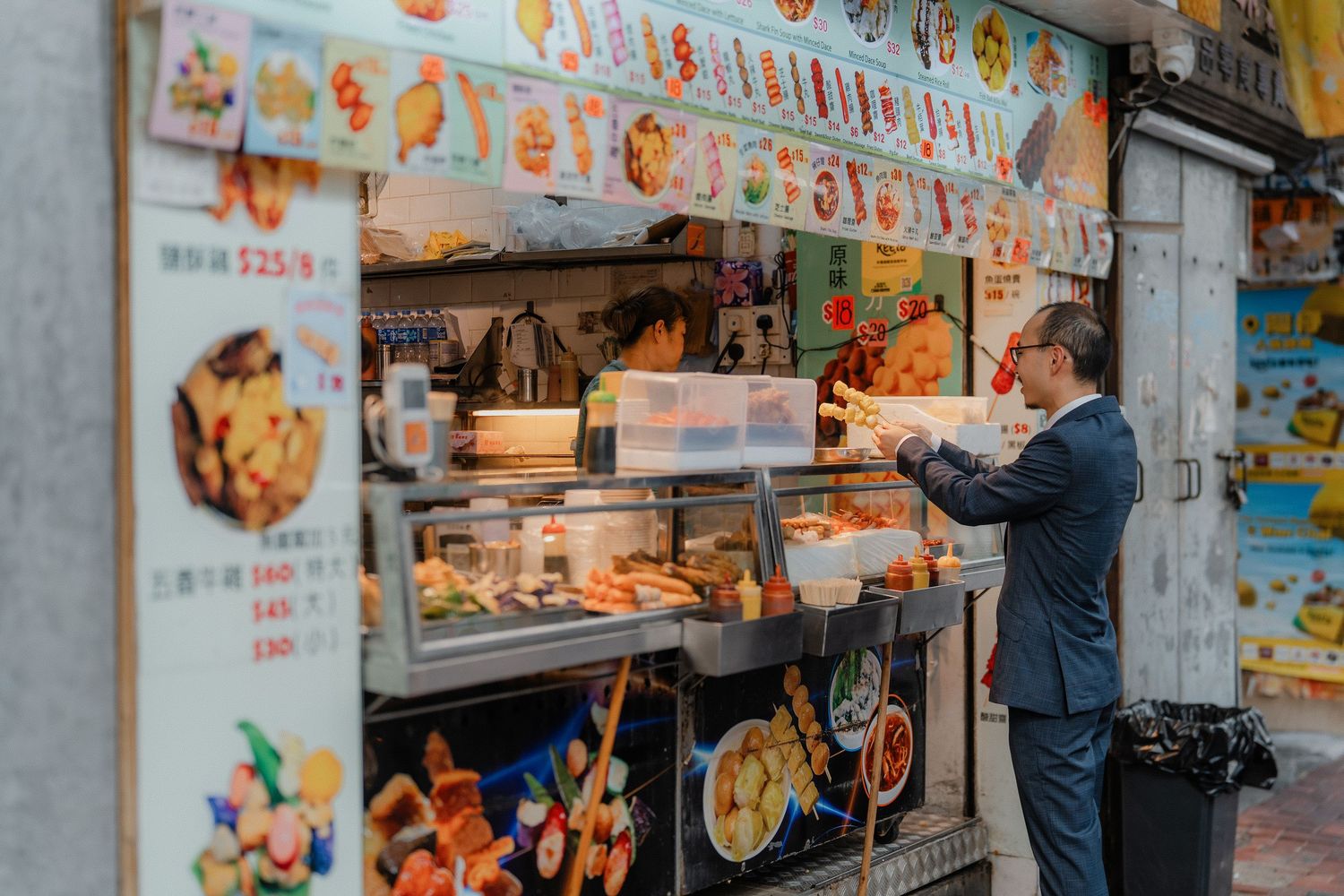 Person in suit ordering from a traditional Hong Kong street food vendor.