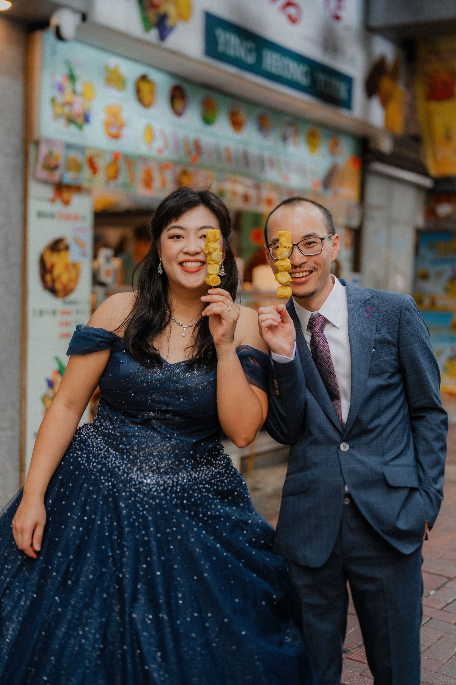 A couple shares a playful moment outside colorful storefronts in Hong Kong.