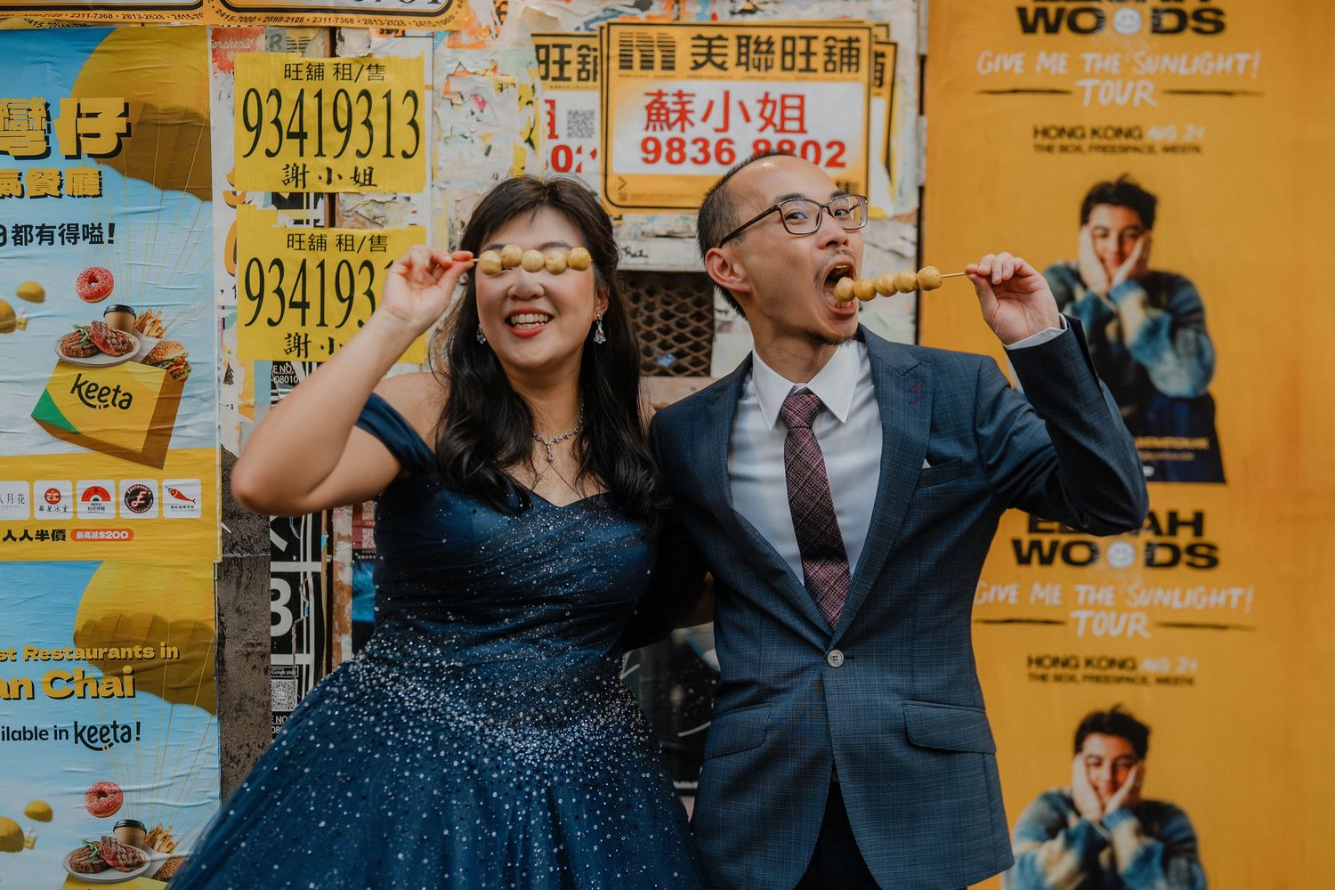 A couple poses playfully against a vibrant yellow wall with Chinese advertisements and posters.