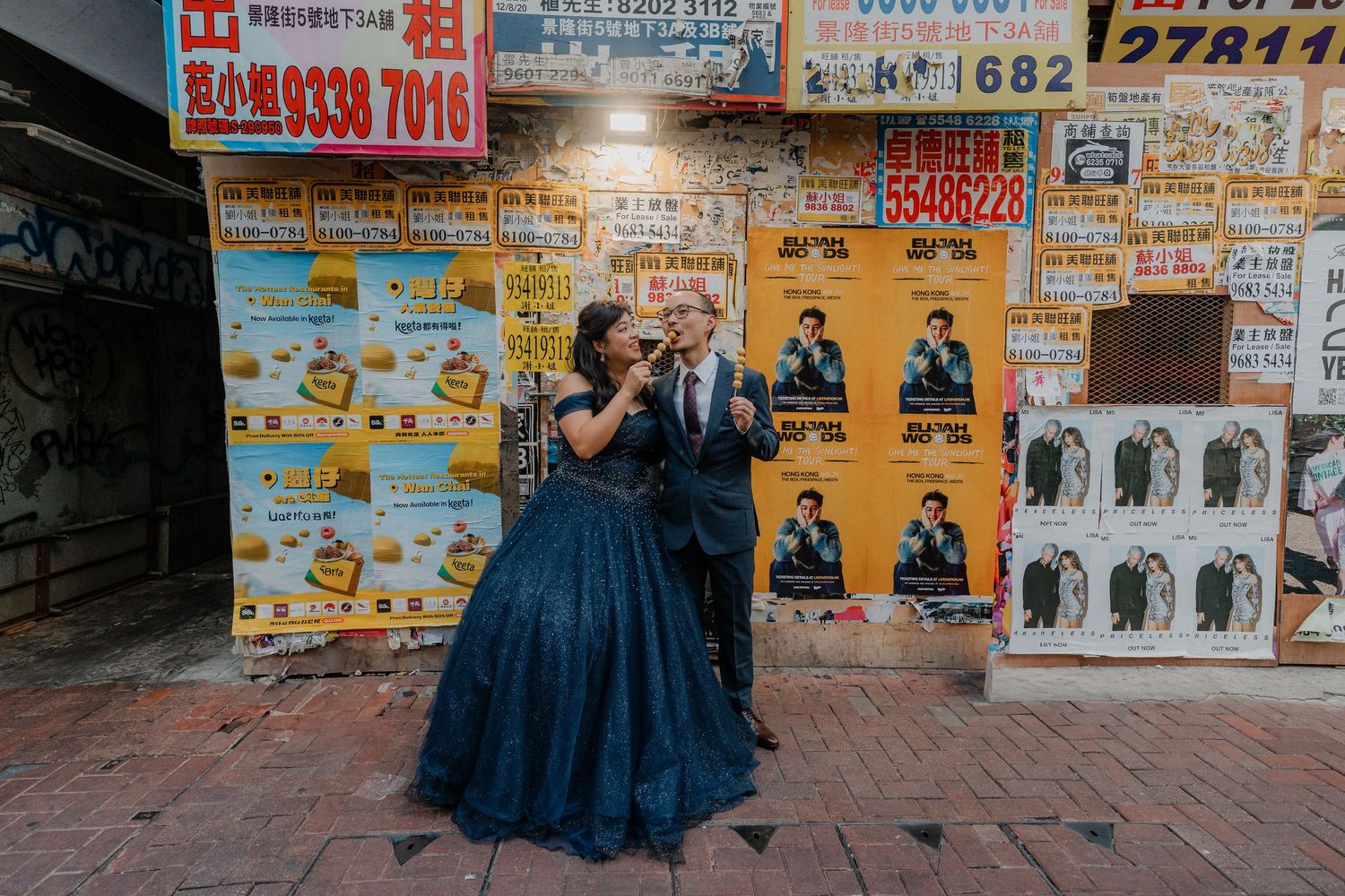 A couple shares a playful moment in front of vibrant Chinese restaurant advertisements and posters.