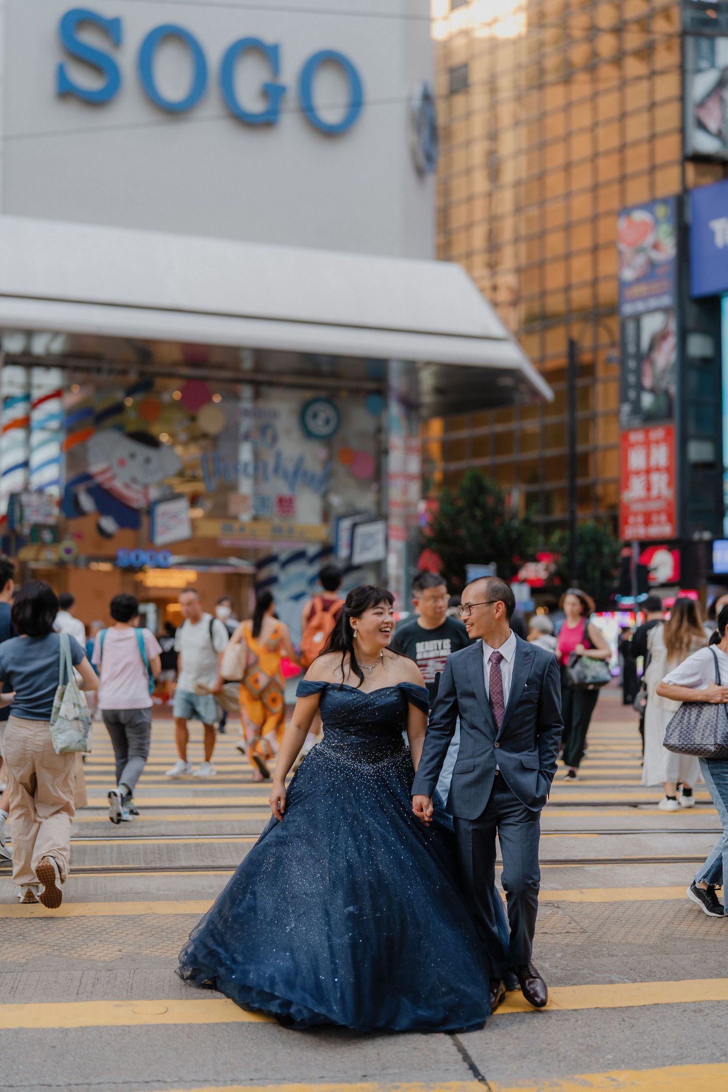 A couple in formal attire dance and twirl in front of the SOGO department store entrance.