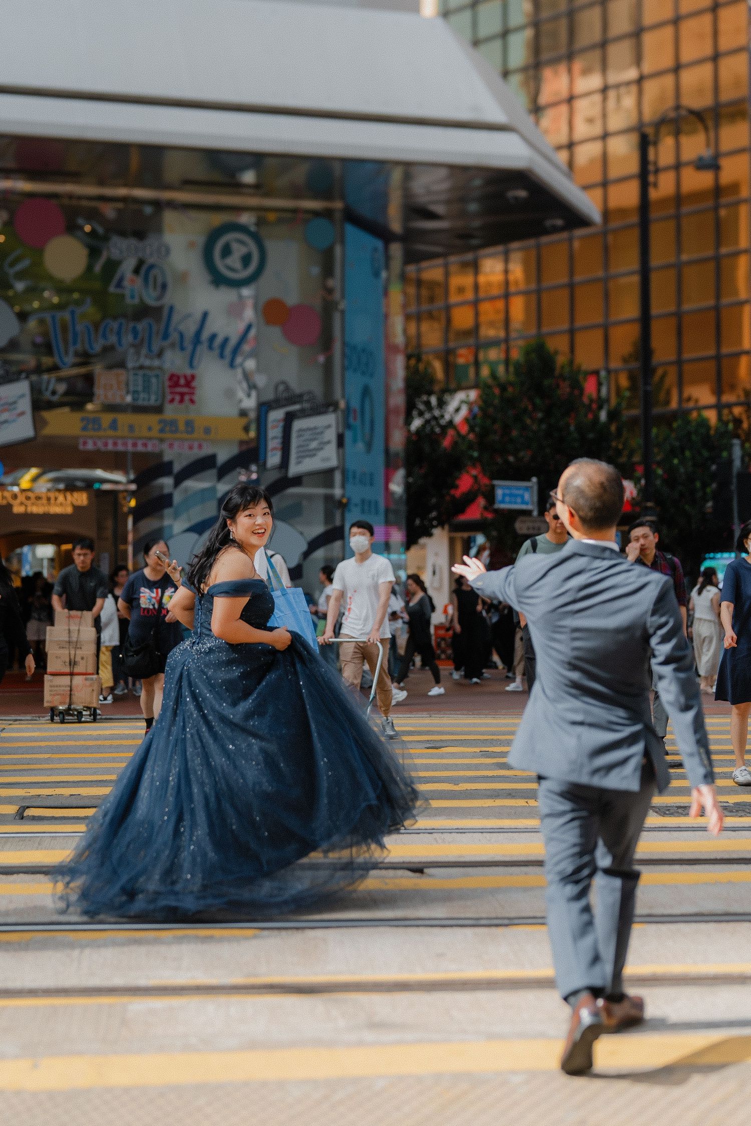 A person in an elegant navy blue gown poses on yellow pedestrian crosswalk stripes in an urban setting.