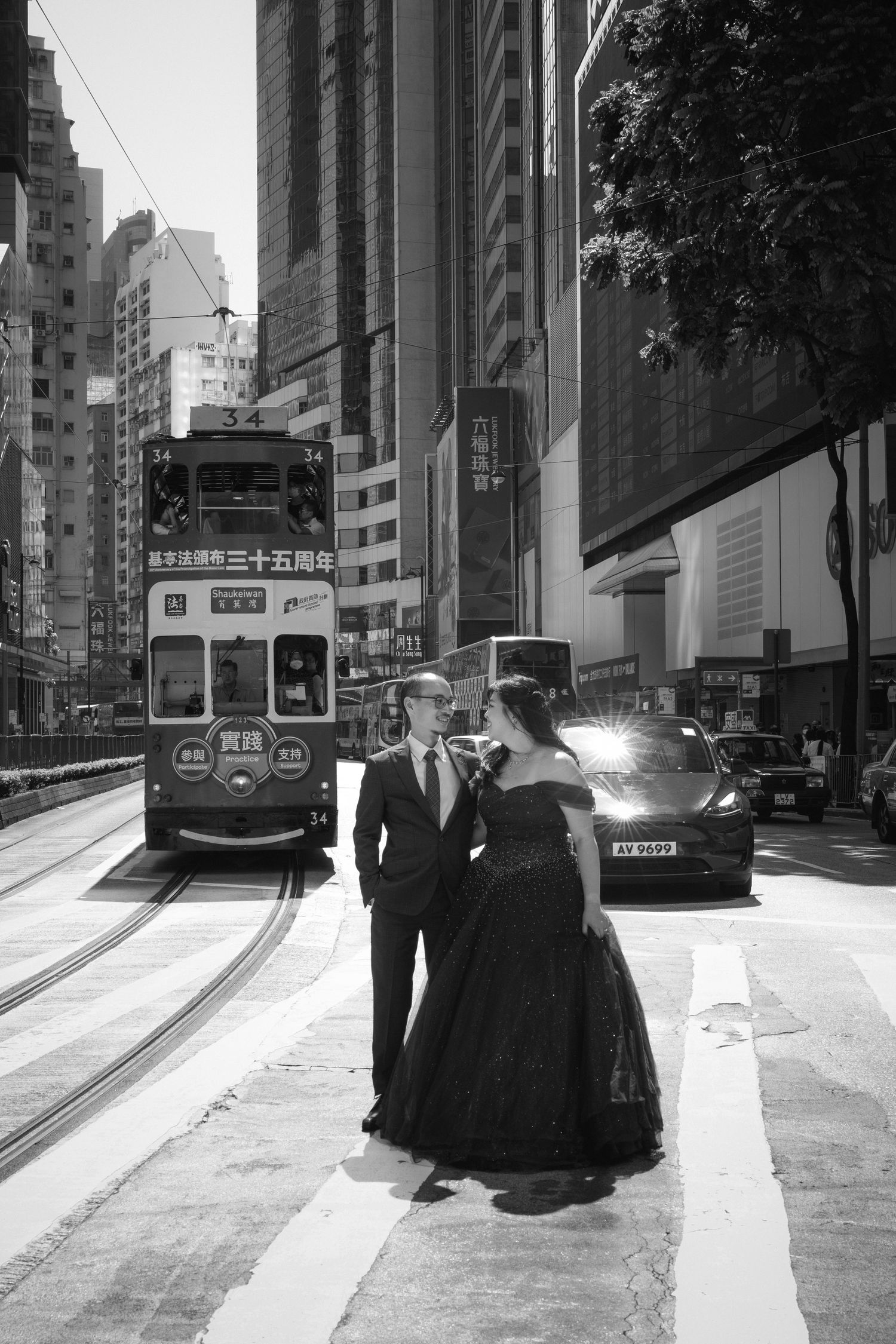 A black and white photo of a couple on a Hong Kong street with passing trams.