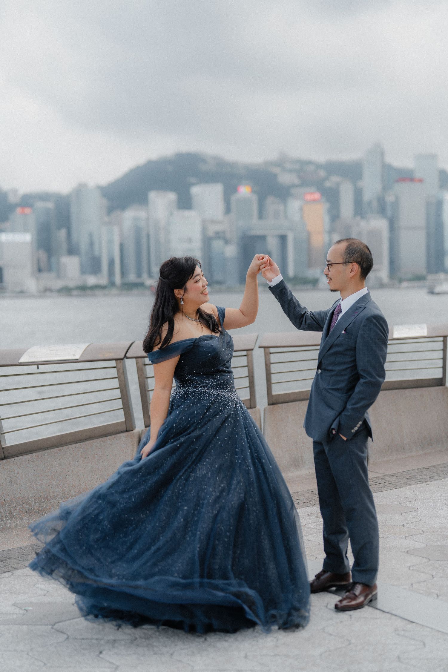 A couple in formal wear dances together against Hong Kong's iconic skyline along Victoria Harbour waterfront.