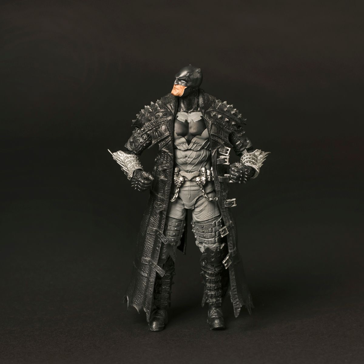 Action figure of Batman wearing dark tactical armor with spikes and metallic details stands against black background.