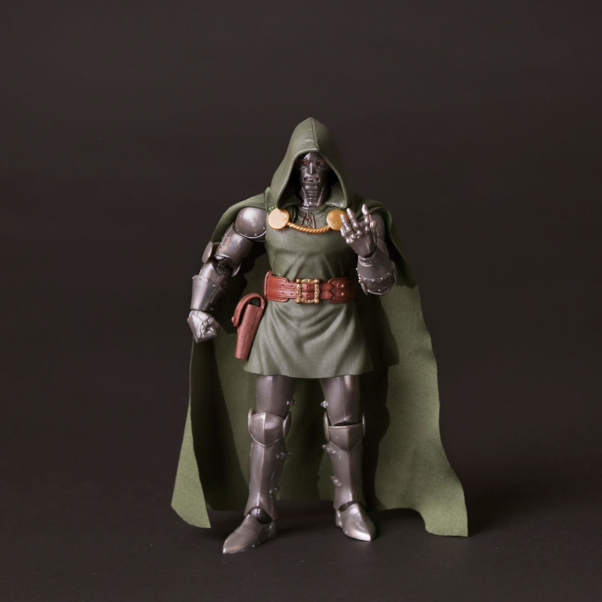 Action figure of Doctor Doom in metallic armor and green hooded cape standing against dark background.
