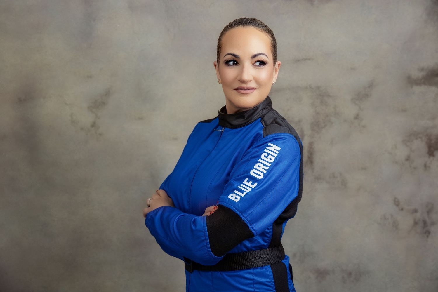 Portrait of someone in athletic wear with arms crossed wearing a blue and black jacket in studio setting.