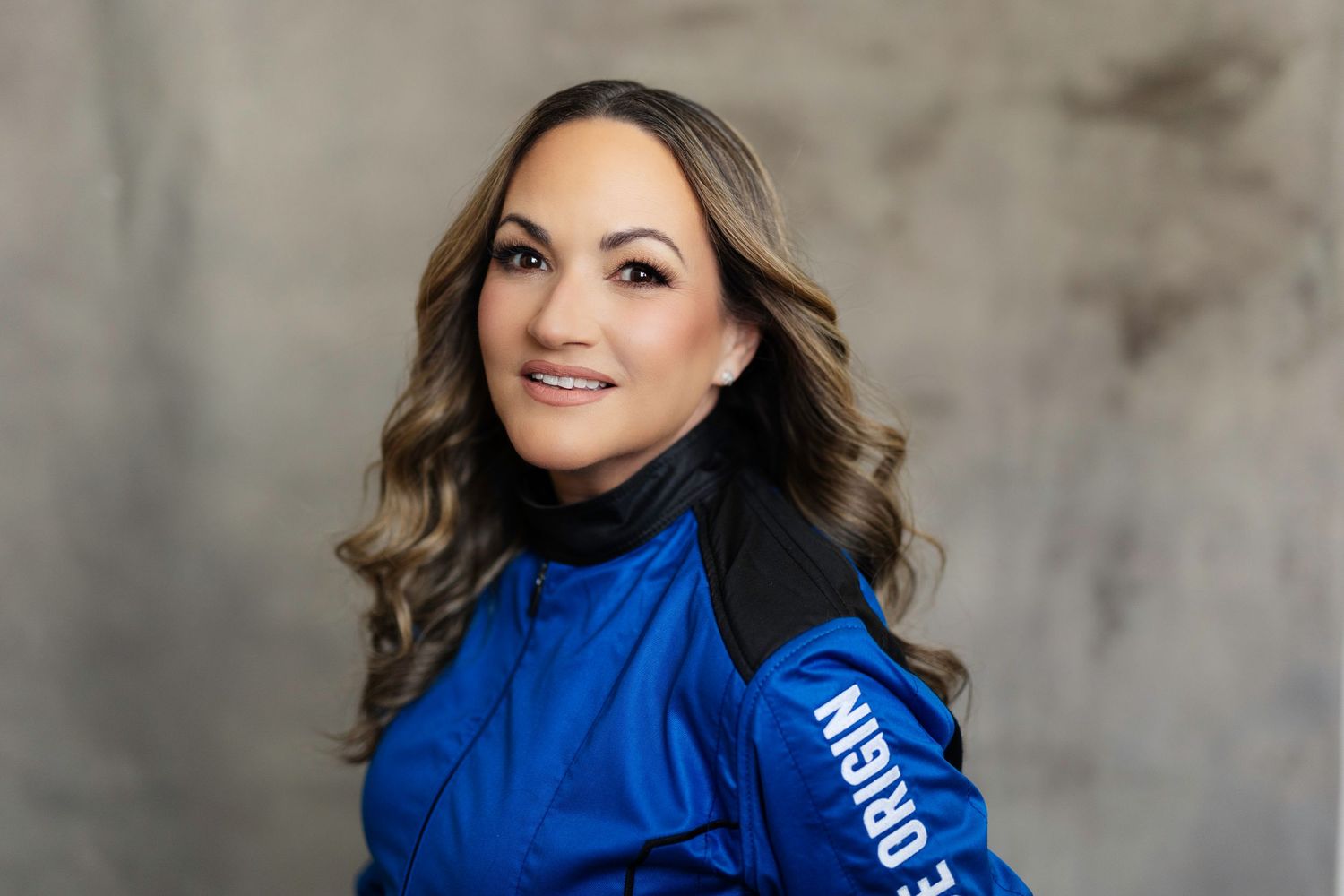 Professional studio portrait of someone in a bright blue athletic jacket against a gray background.