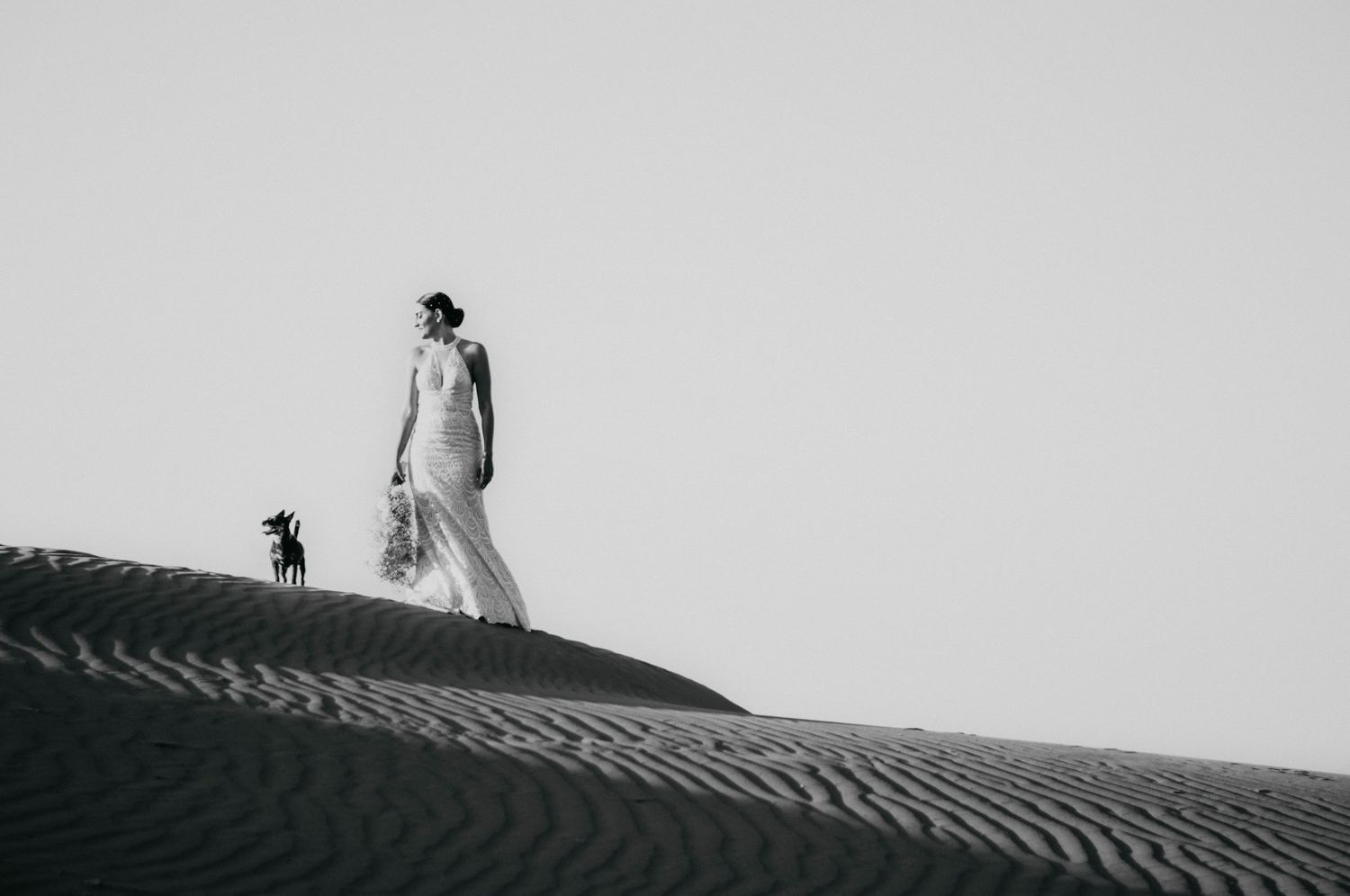 A couple poses for a series of romantic wedding portraits on a bright beach setting wearing black and white attire.
