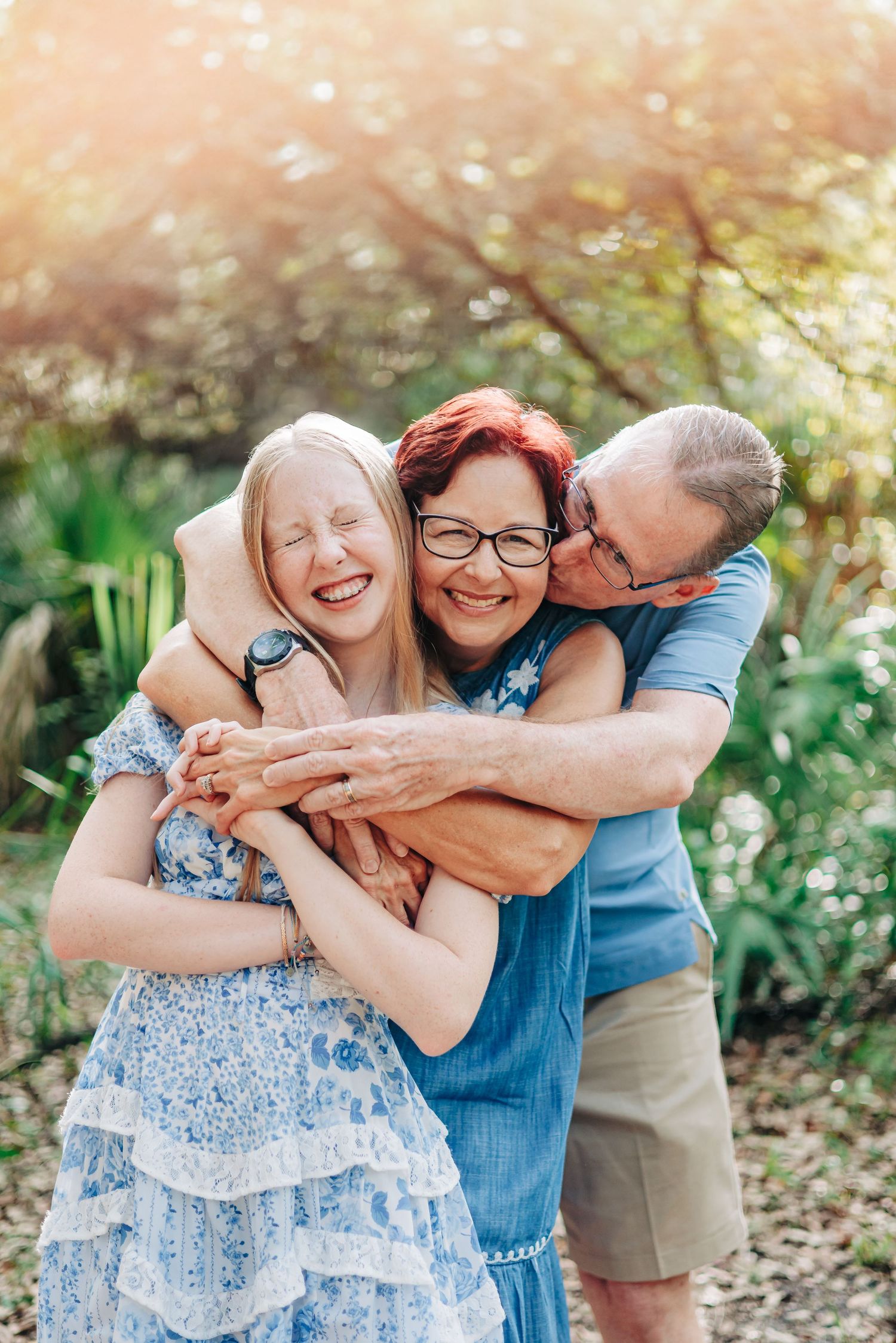 A joyful family embraces together outdoors in a garden setting with soft sunlight filtering through trees.