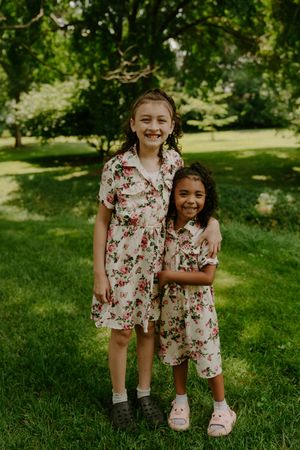 Two children in matching floral dresses share a sweet hug on green grass.
