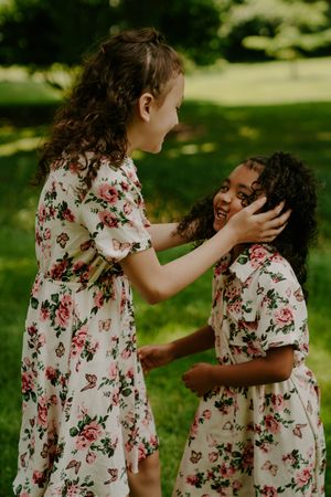 Two children in matching floral dresses share playful moments outdoors.