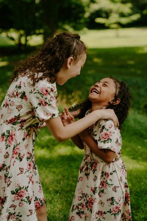 Children in floral dresses laugh and play together in a sunlit garden setting.
