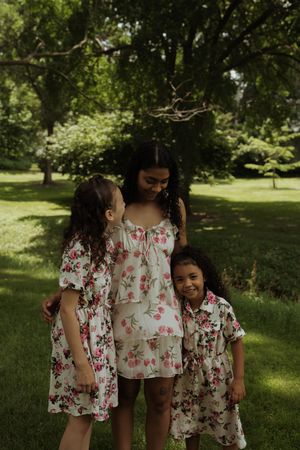 Children wearing matching floral dresses share tender moment in sunny park.
