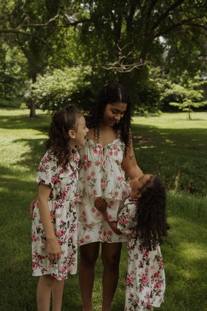 Family group wearing coordinated floral outfits poses in green park setting.