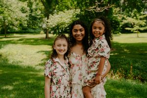 Three people in matching floral print dresses share joyful moments together in a park.