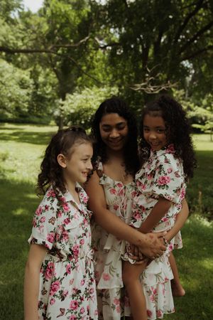 Two children in matching floral dresses share a playful moment in a sunny park setting.