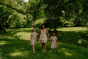 Three figures in matching floral outfits walk together through a sunlit park.